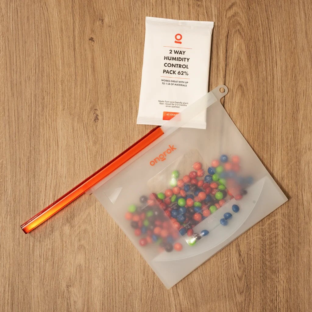 ONGROK 67 Gram Humidity Pack on a wood table beside a clear bag of colorful candy and an orange straw