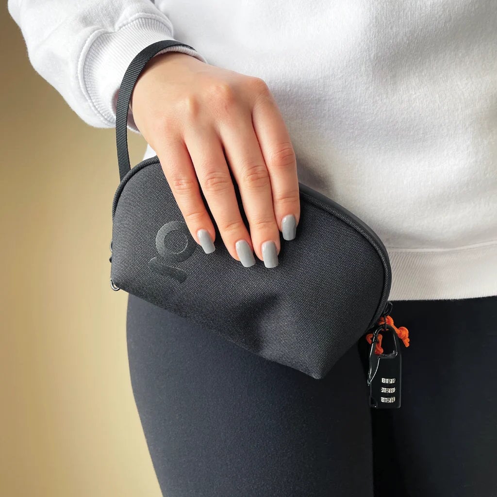 Hand holding a black ONGROK Carbon-lined Wrist Bag against black leggings, combo lock on the zipper