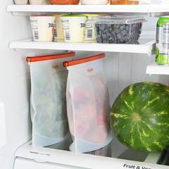 ONGROK Silicone Oven & Storage Bags, large 2 pack, holding greens and tomatoes in a fridge beside a watermelon